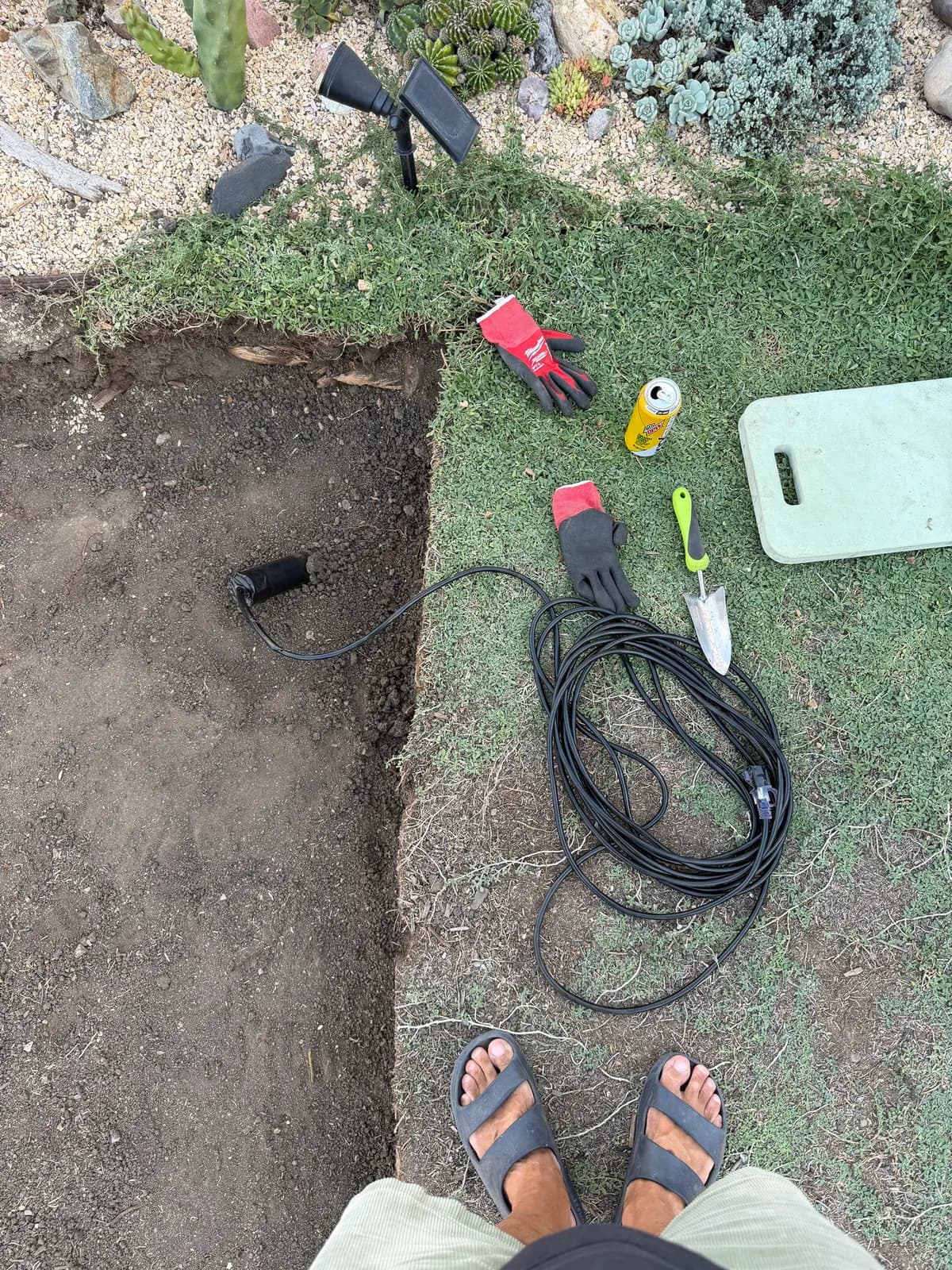 A low-voltage lighting cable uncovered at the edge of the dig