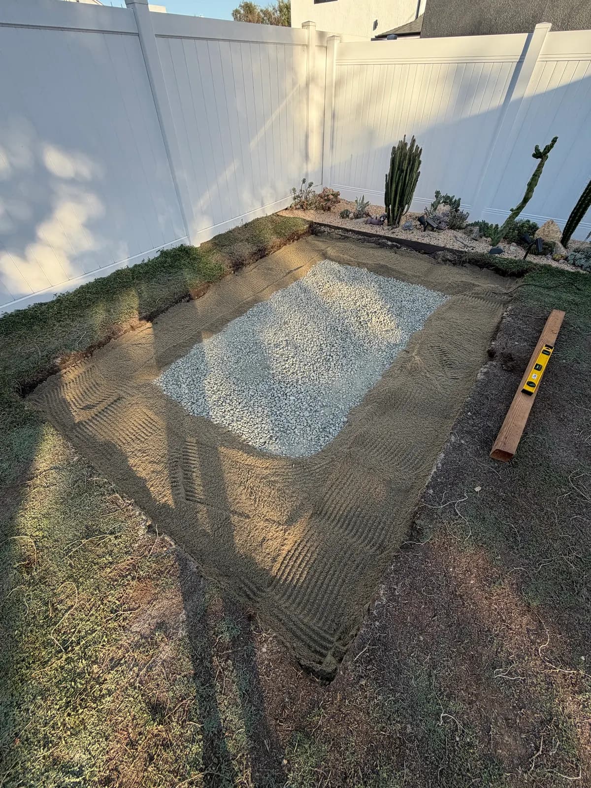 Sand raked around the full perimeter of the gravel pad, a timber and level beside it