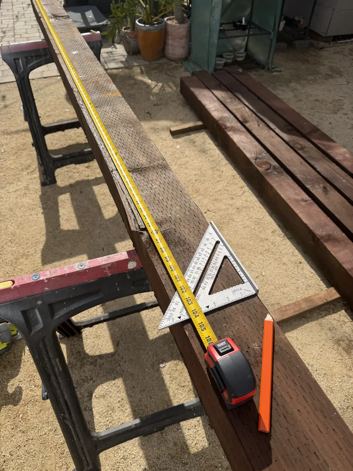 A tape measure run down a 6×6 on sawhorses to about 105″, with a speed square and carpenter's pencil at the end