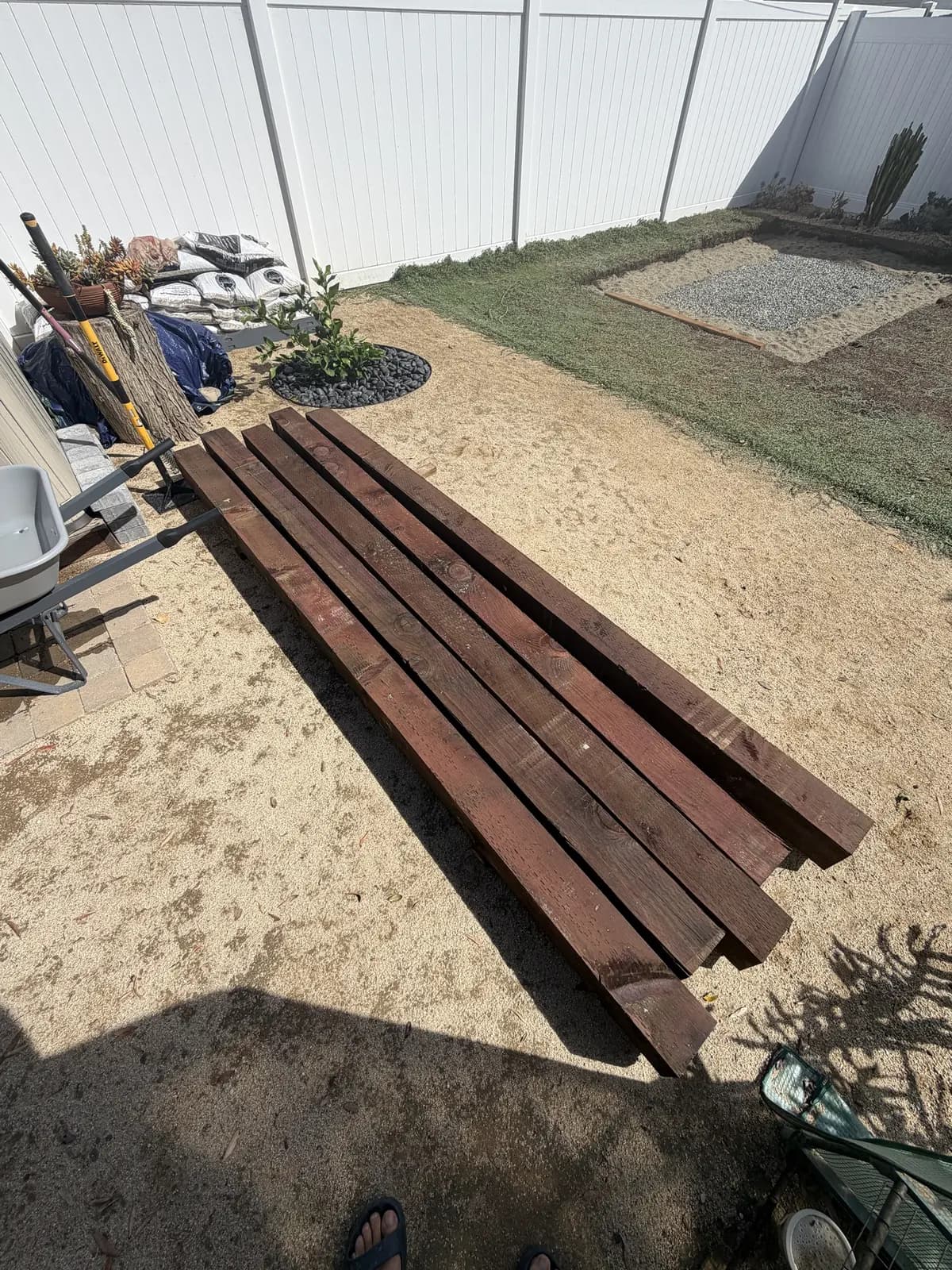 Five stained 6×6 timbers laid side by side on the decomposed granite beside the pad